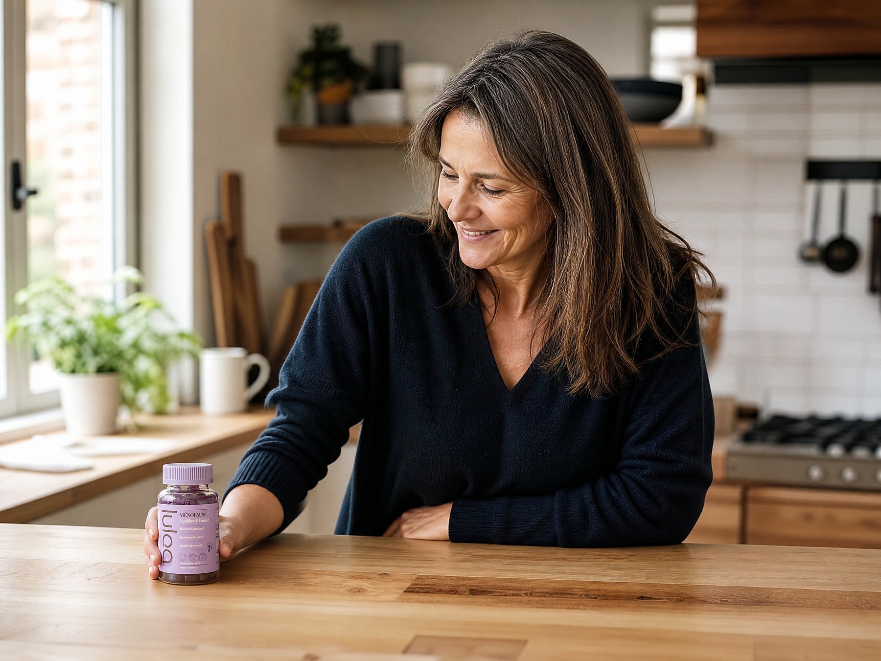 Une femme dans sa cuisine regarde son pot de gummies Lulea Ménopause